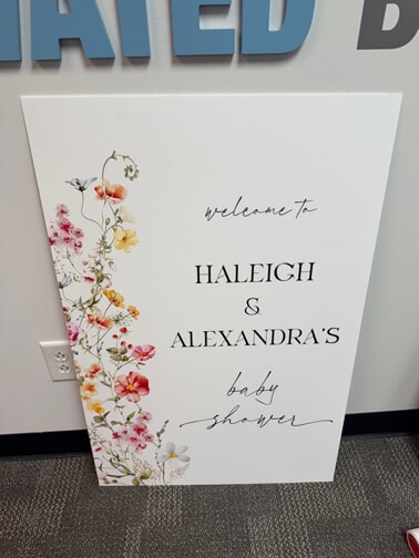 An image of a summer themed baby shower poster with pink and yellow flowers.